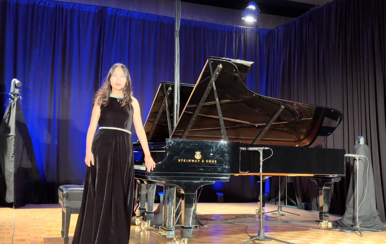 Meining Wu on stage beside the piano under the spotlight at the Young Artist Guild Induction Concert